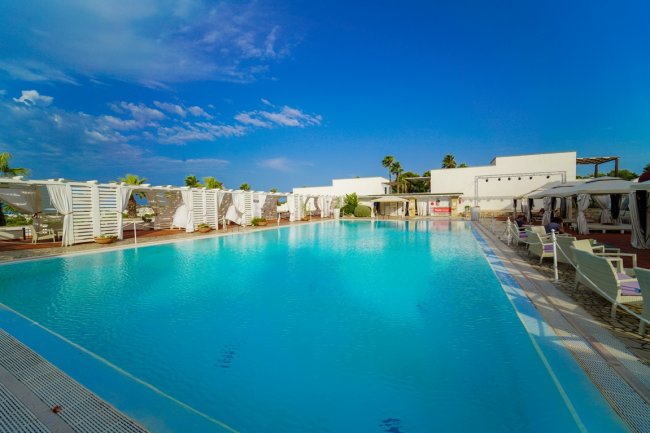 Piscina azzurra con lettini e cielo blu.