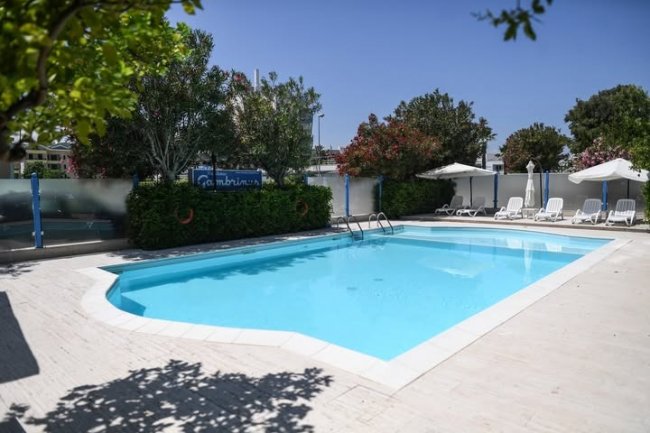 Una piscina con lettini e ombrelloni bianchi sotto un cielo sereno.