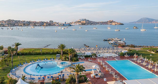 Vista aerea di piscine, ombrelloni e barche nella baia.