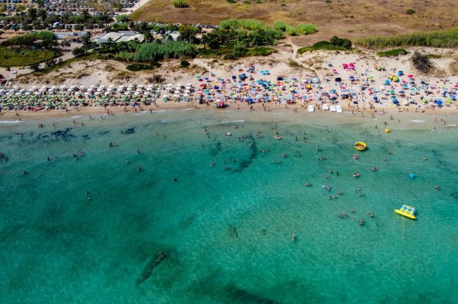 Spiaggia affollata con mare limpido e ombrelloni colorati.