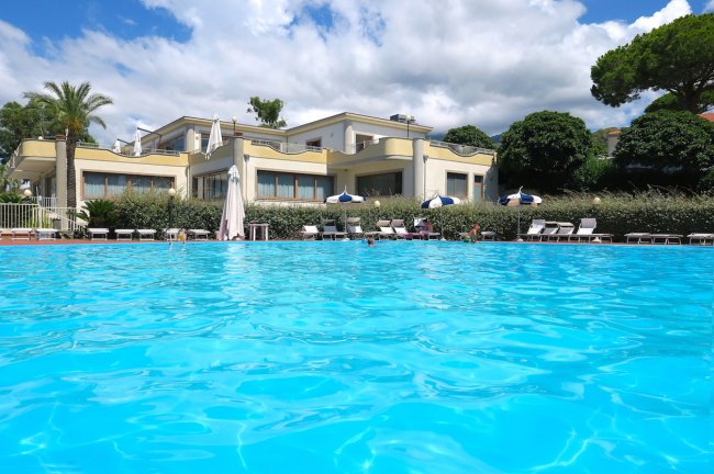 Piscina azzurra davanti a una villa con terrazze e lettini.