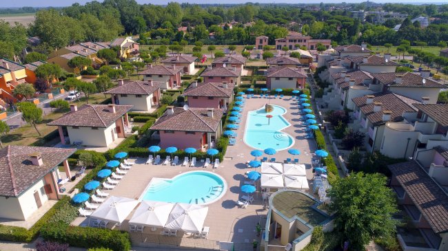 Vista aerea di un villaggio con piscine e ombrelloni.