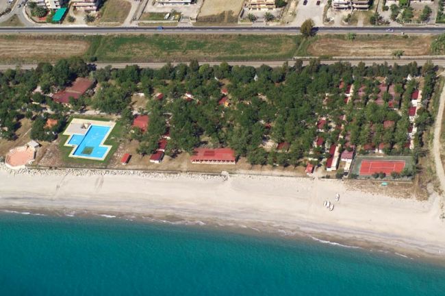 Spiaggia e complesso turistico con piscina e campi sportivi circondati da alberi.