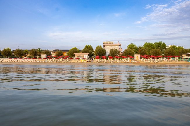 Spiaggia con ombrelloni rossi vista dal mare.