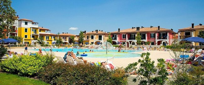 Persone rilassate attorno a una piscina circondata da edifici colorati.