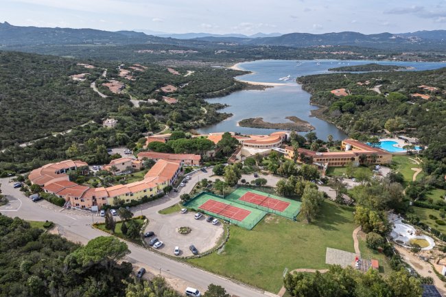 Vista di un complesso con campi da tennis e mare in lontananza.