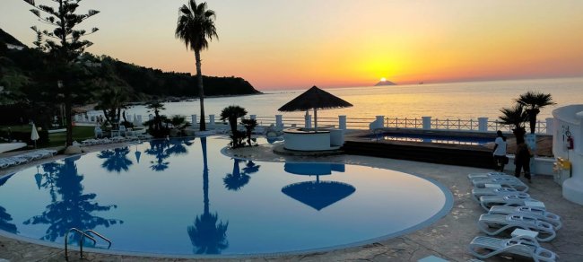 Piscina al tramonto, vista mare con palme.