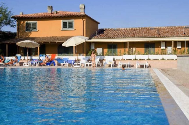 Piscina con ombrelloni e lettini, edificio arancione sullo sfondo.