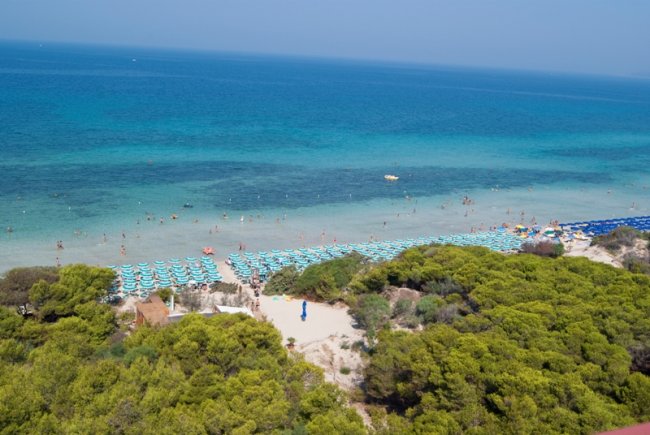 Spiaggia affollata con sedie a sdraio e ombrelloni.