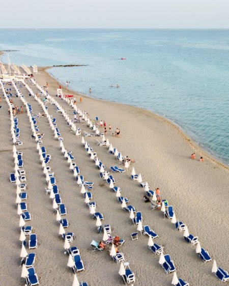 Spiaggia con file di sedie a sdraio blu e bianche.