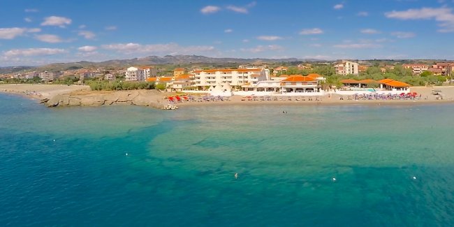 Vista aerea di un hotel sul mare con spiaggia e ombrelloni colorati.