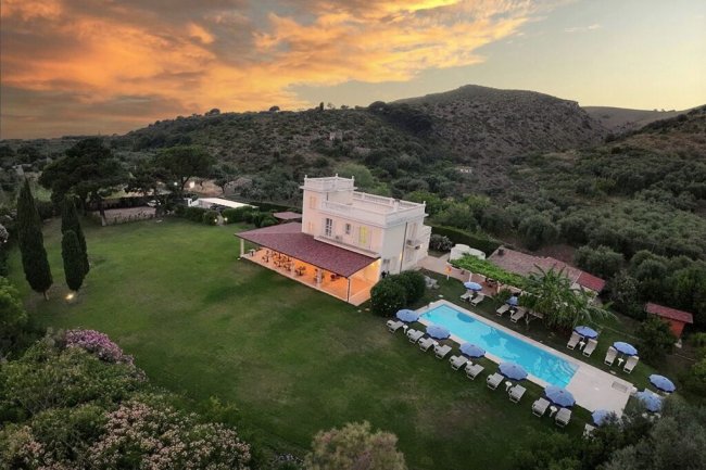 Villa con piscina al tramonto, su uno sfondo collinare.