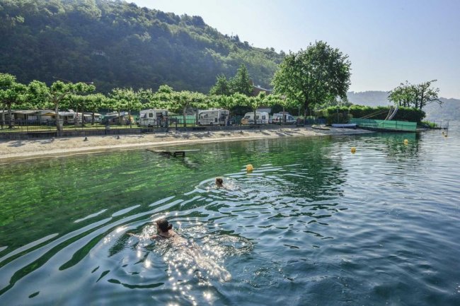 Persone nuotano in un lago vicino a camper.