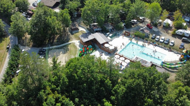 Vista aerea di un campeggio con piscina tra alberi.