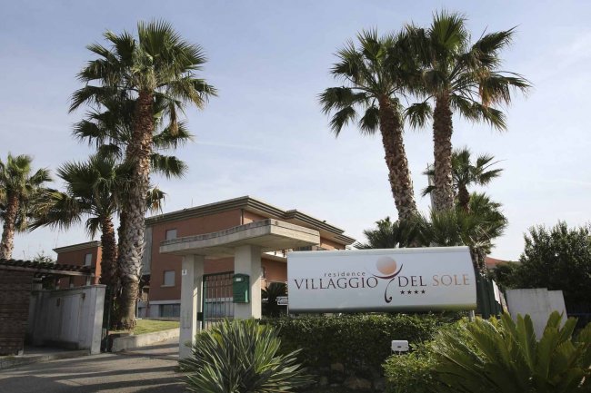 Ingresso del Villaggio del Sole con palme e vegetazione.