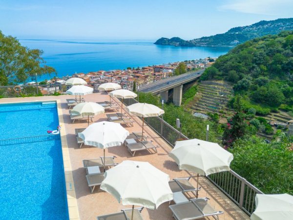 Vista mare da piscina con ombrelloni e lettini.
