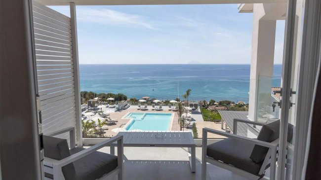 Vista su piscina e mare da balcone con sedie.