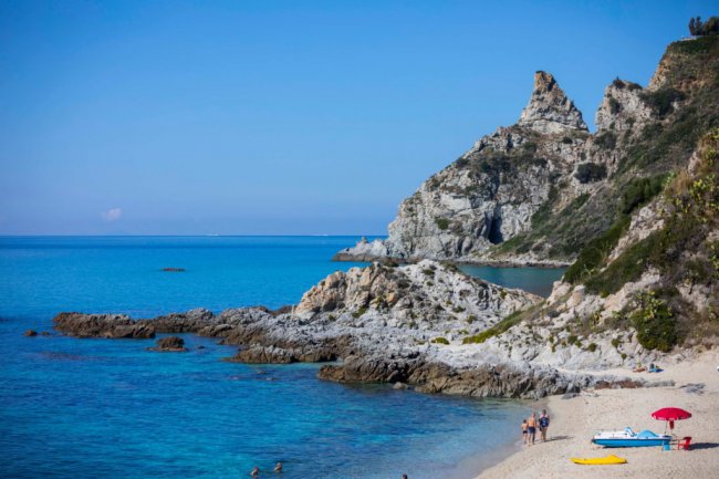 Spiaggia rocciosa con mare blu e promontori.