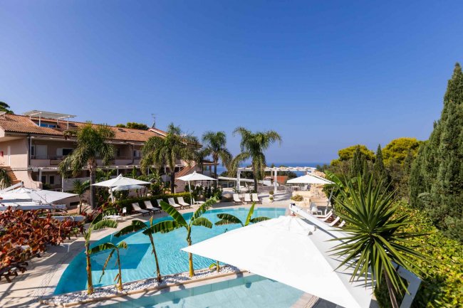 Piscina con palme, ombrelloni e cielo blu.