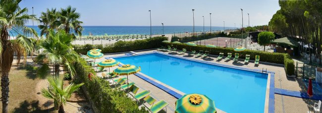 Piscina circondata da sdraio e ombrelloni, vicino al mare.