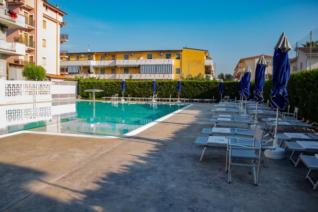 Piscina esterna con lettini e ombrelloni blu.