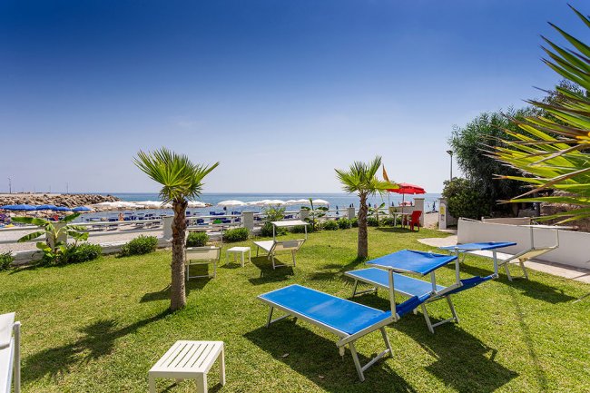 Giardino con lettini blu e vista mare.