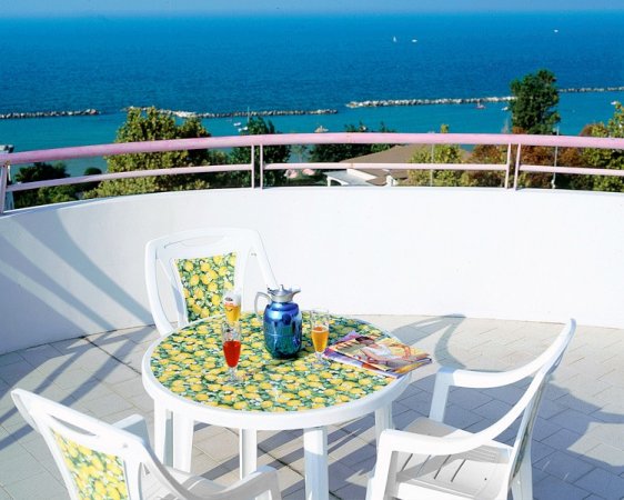Tavolo bianco su terrazza con vista mare e bevande.