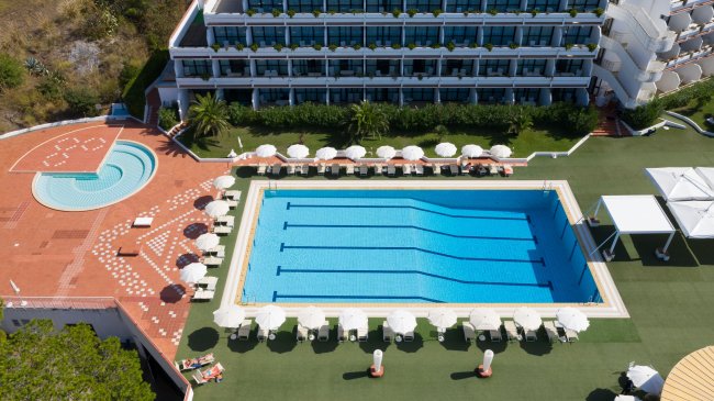 Piscina rettangolare circondata da lettini e ombrelloni.