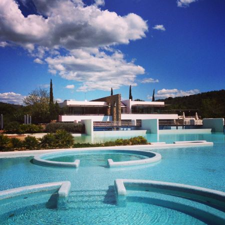 Piscina moderna con vegetazione e cielo nuvoloso.