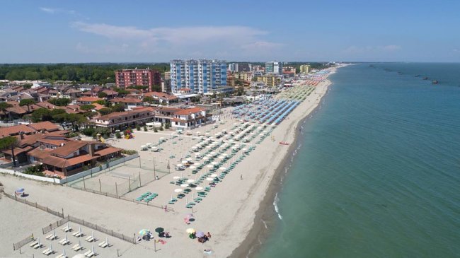 Spiaggia con ombrelloni colorati, mare limpido e edifici sullo sfondo.
