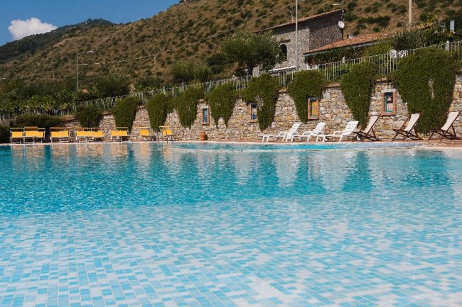 Piscina con bordo piastrellato, sdraio e collina sullo sfondo.