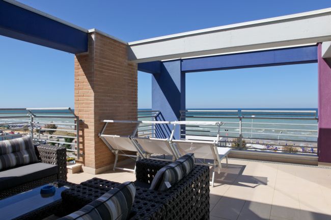 Terrazza moderna con sedie e divani, vista su mare e cielo blu.