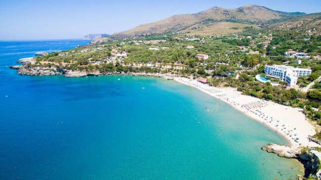 Spiaggia sabbiosa con mare blu e colline verdi.