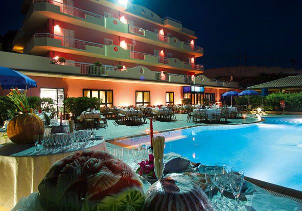 Una piscina di notte con un edificio arancione illuminato e decorazioni natalizie.