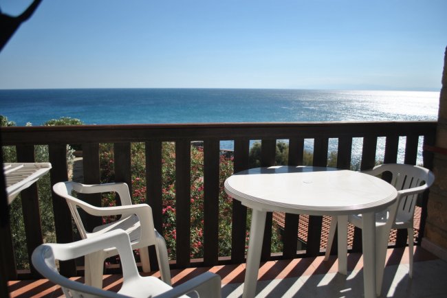Tavolo e sedie bianche su un balcone con vista mare.