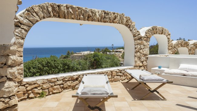 Letti prendisole sotto un arco con vista mare.