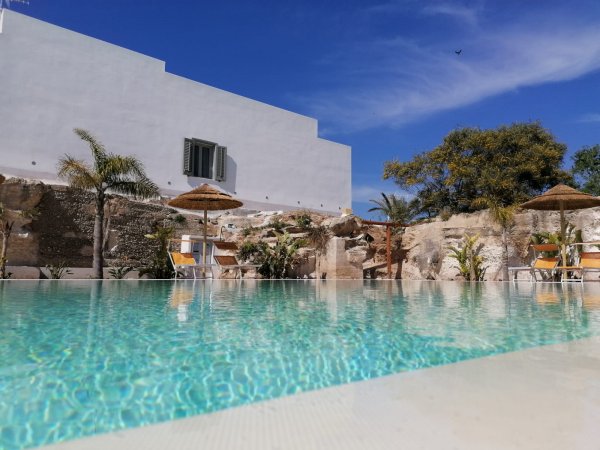 Piscina con ombrelloni di paglia e edificio bianco.