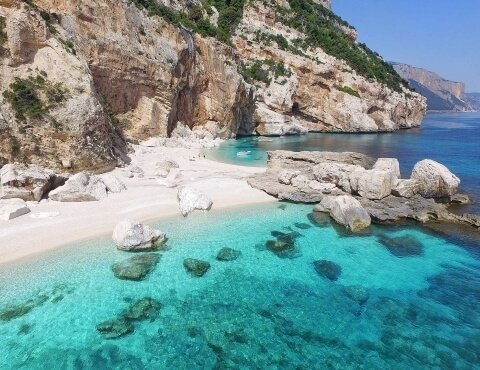 Spiaggia con acqua cristallina e scogliere rocciose.