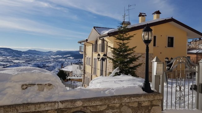Casa gialla innevata con montagne sullo sfondo.