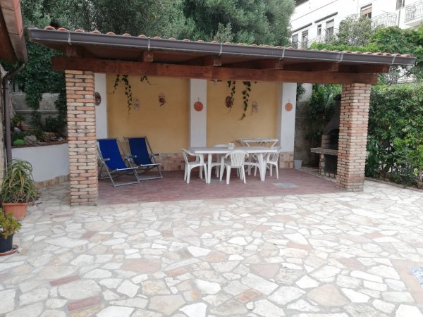 Patio con tavolo, sedie bianche e sdraio.