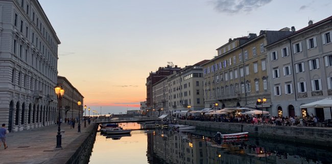 Tramonto su canale con edifici e luci accese.