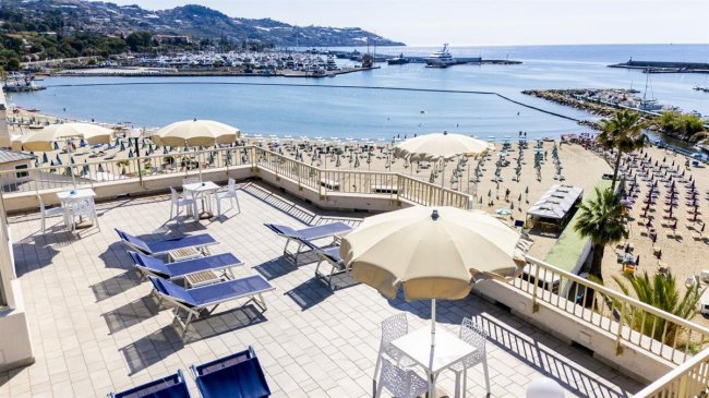 Terrazza con lettini e ombrelloni, vista sul porto.