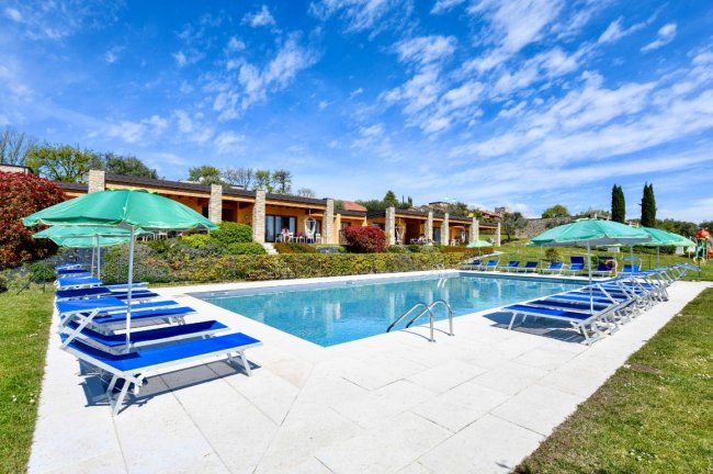 Piscina rettangolare con lettini blu e ombrelloni verdi.