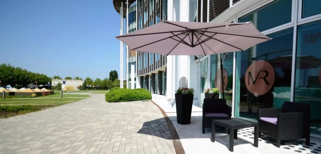 Esterno con ombrellone, tavoli e sedie vicino a un edificio moderno.