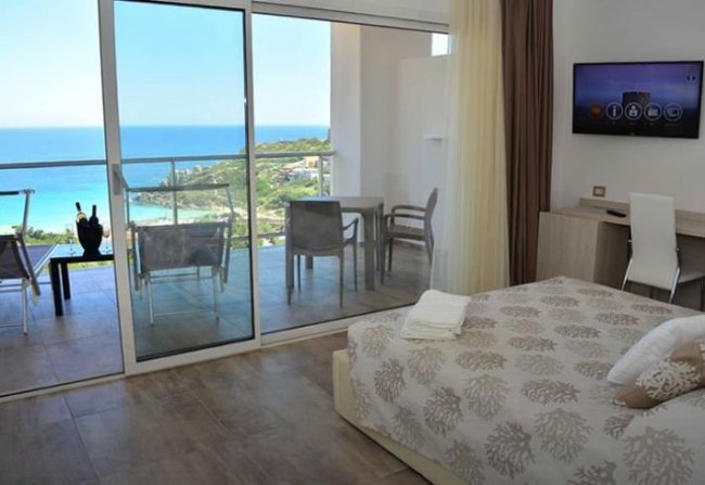 Camera da letto luminosa con balcone e vista sul mare.