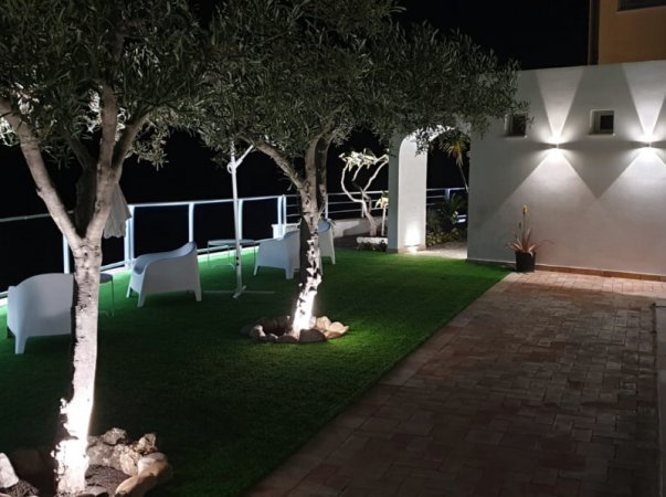 Area con sedie bianche, alberi e luci notturne.