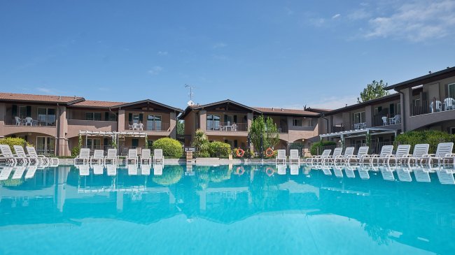 Piscina con sedie a sdraio e edifici residenziali sullo sfondo.