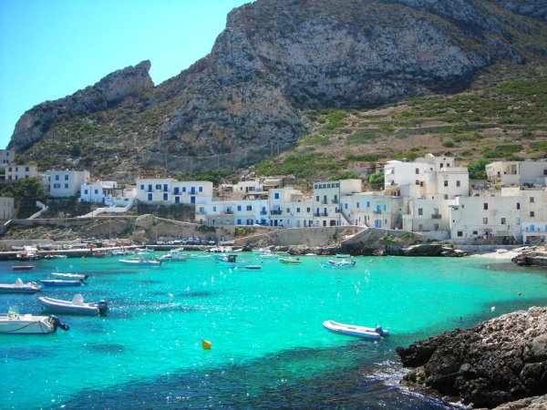 Baia con case bianche, mare turchese e barchette.