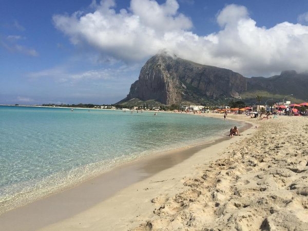 Spiaggia sabbiosa con mare calmo e una montagna in lontananza.