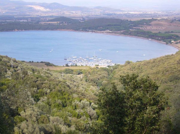 Vista panoramica di una baia con barche circondata da colline verdi.